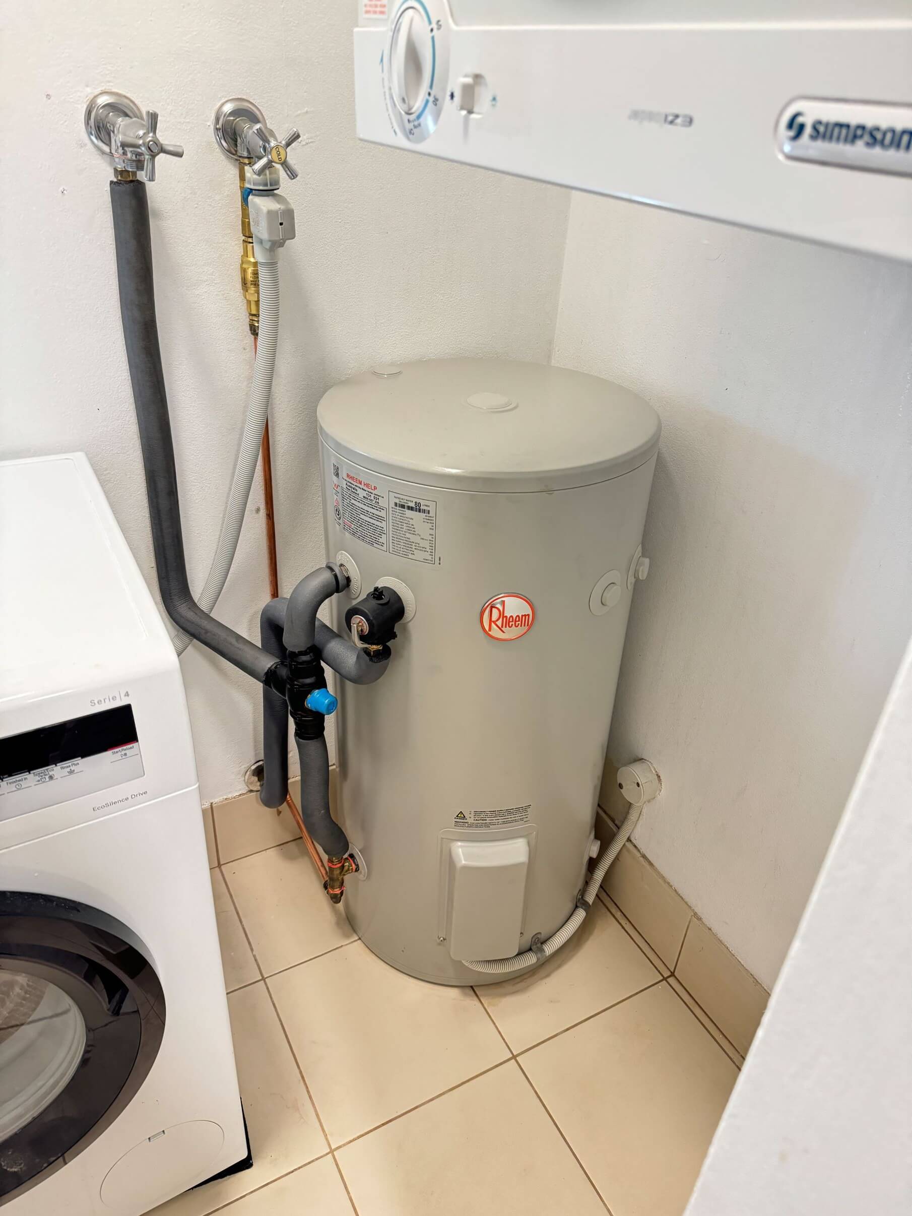 A new electric hot water heater neatly installed in a Mount Colah laundry beside a washing machine.